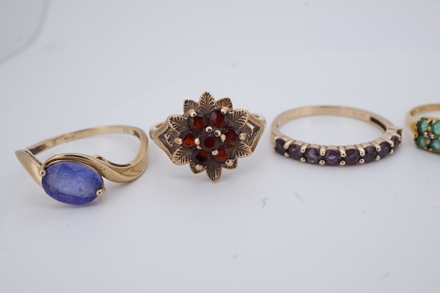 Seven gem-set rings, comprising: a faceted opal and diamond ring; a kunzite and colourless paste cluster ring; a garnet cluster ring; a blue zircon and colourless paste ring; and a tanzanite ring, all mounted in 9ct gold